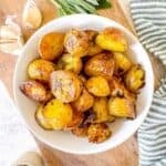 roasted sage potatoes in a white bowl next to garlic cloves and sage leaves.