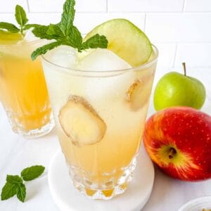apple juice mocktails in two glasses next to fresh apples and mint leaves.