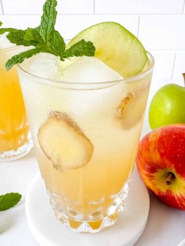 apple juice mocktails in two glasses next to fresh apples and mint leaves.