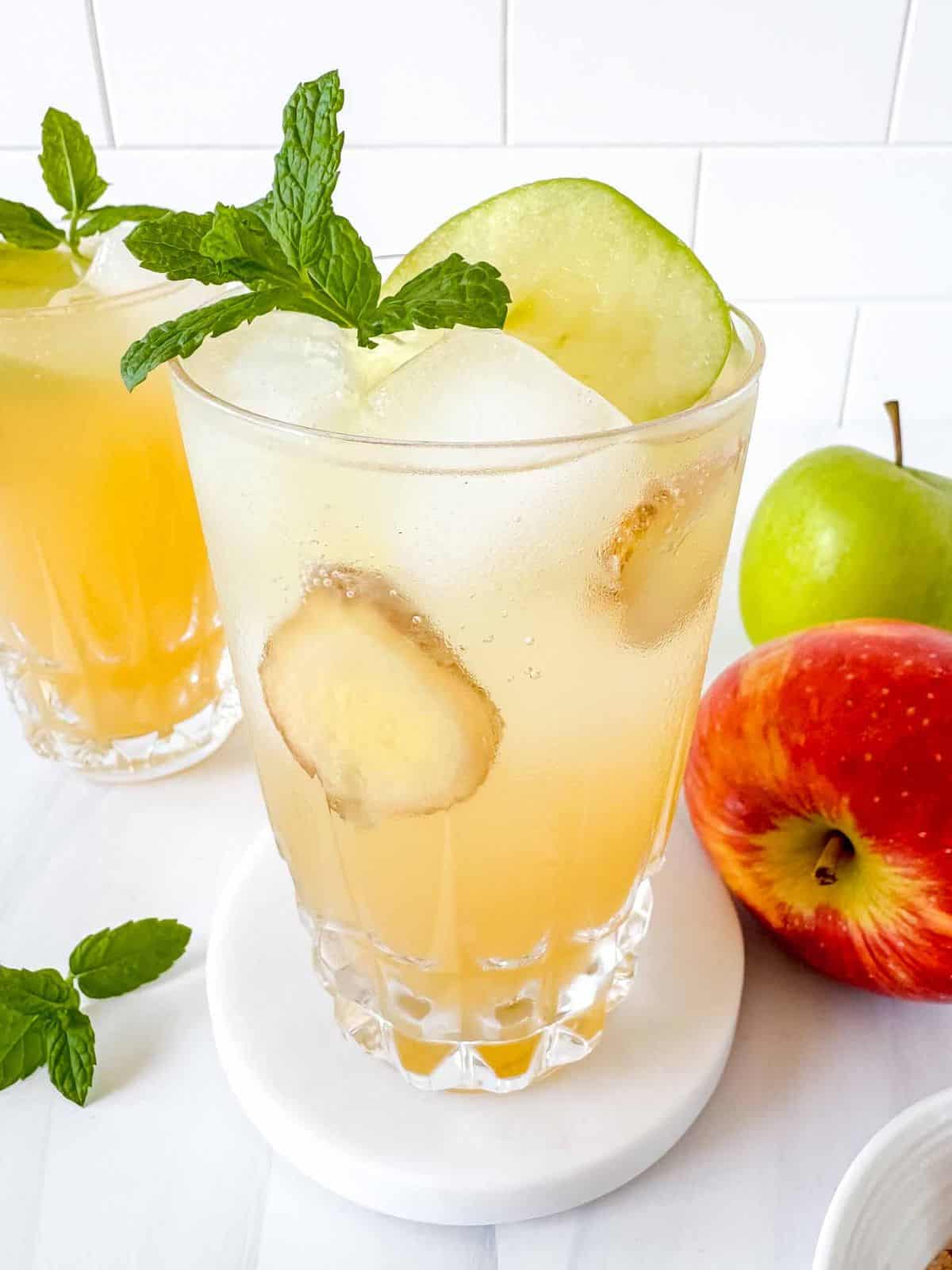 apple juice mocktail in two glasses next to fresh apples and mint leaves.