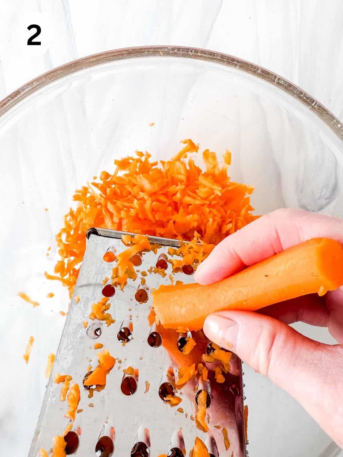 carrots being grated into a glass bowl labelled number two.