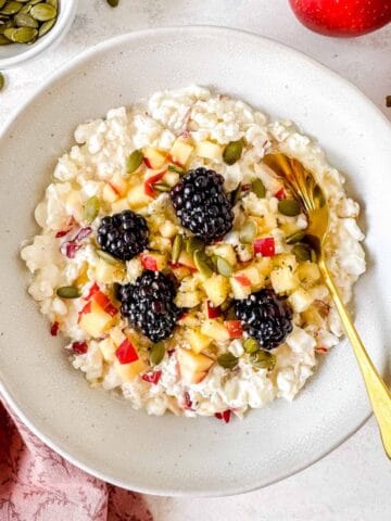 cottage cheese and apple bowl topped with diced apples, blackberries and seeds.