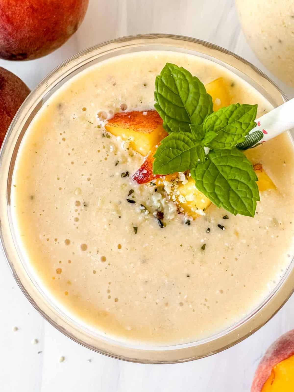 peach smoothie without yogurt in a glass topped with fresh peach pieces and mint leaves.