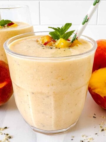peach protein smoothie without yogurt in two glasses next to fresh peaches.