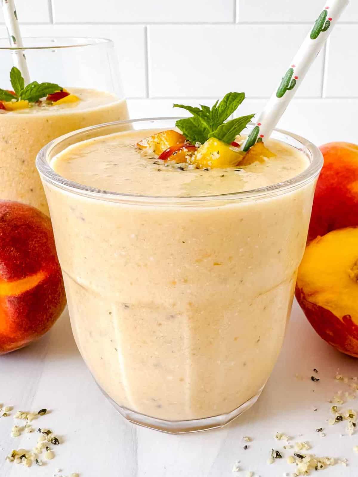 peach protein smoothie without yogurt or banana in two glasses next to fresh peaches.