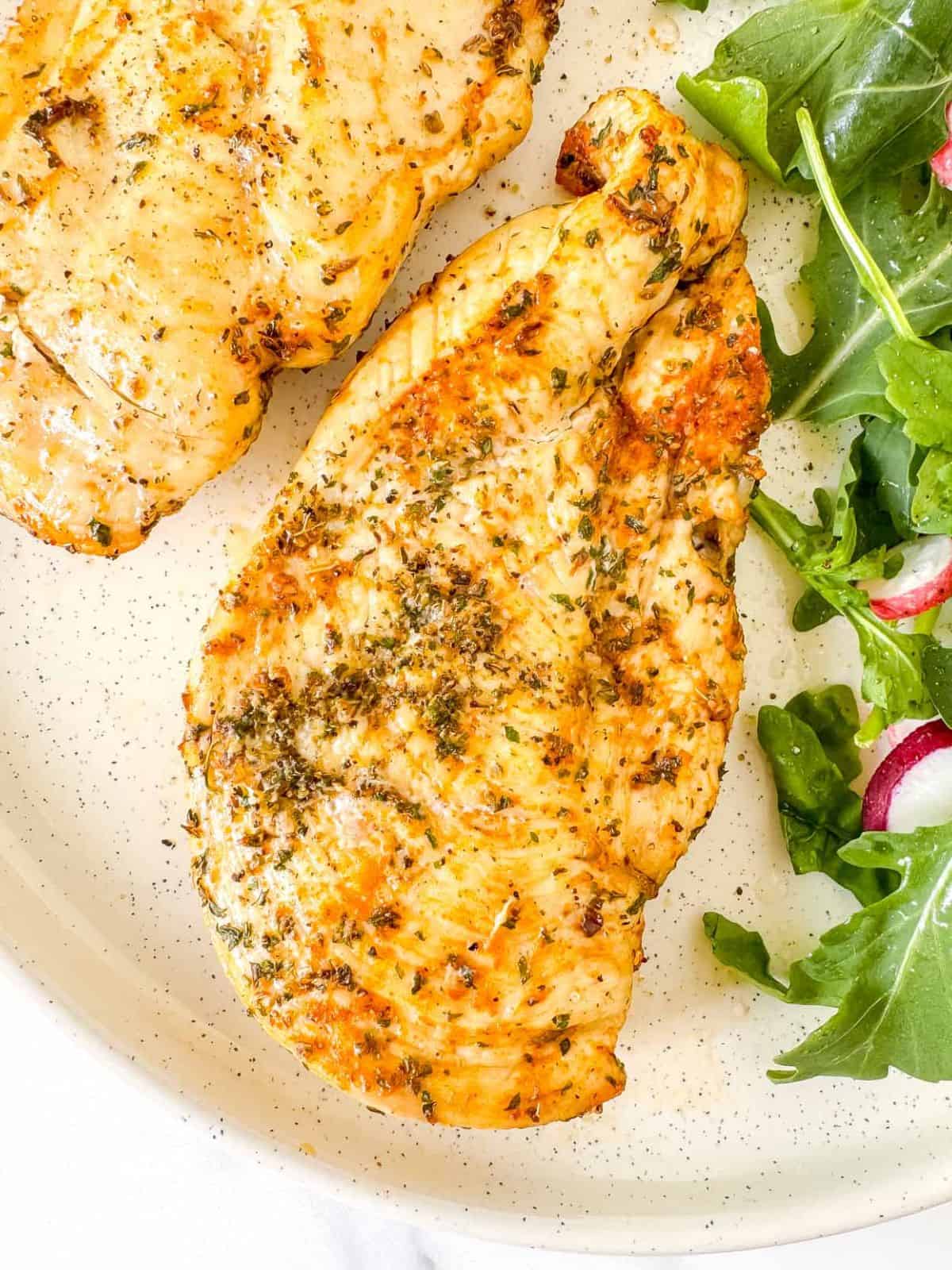 two pieces of air fried thin sliced chicken breast on a plate with arugula.