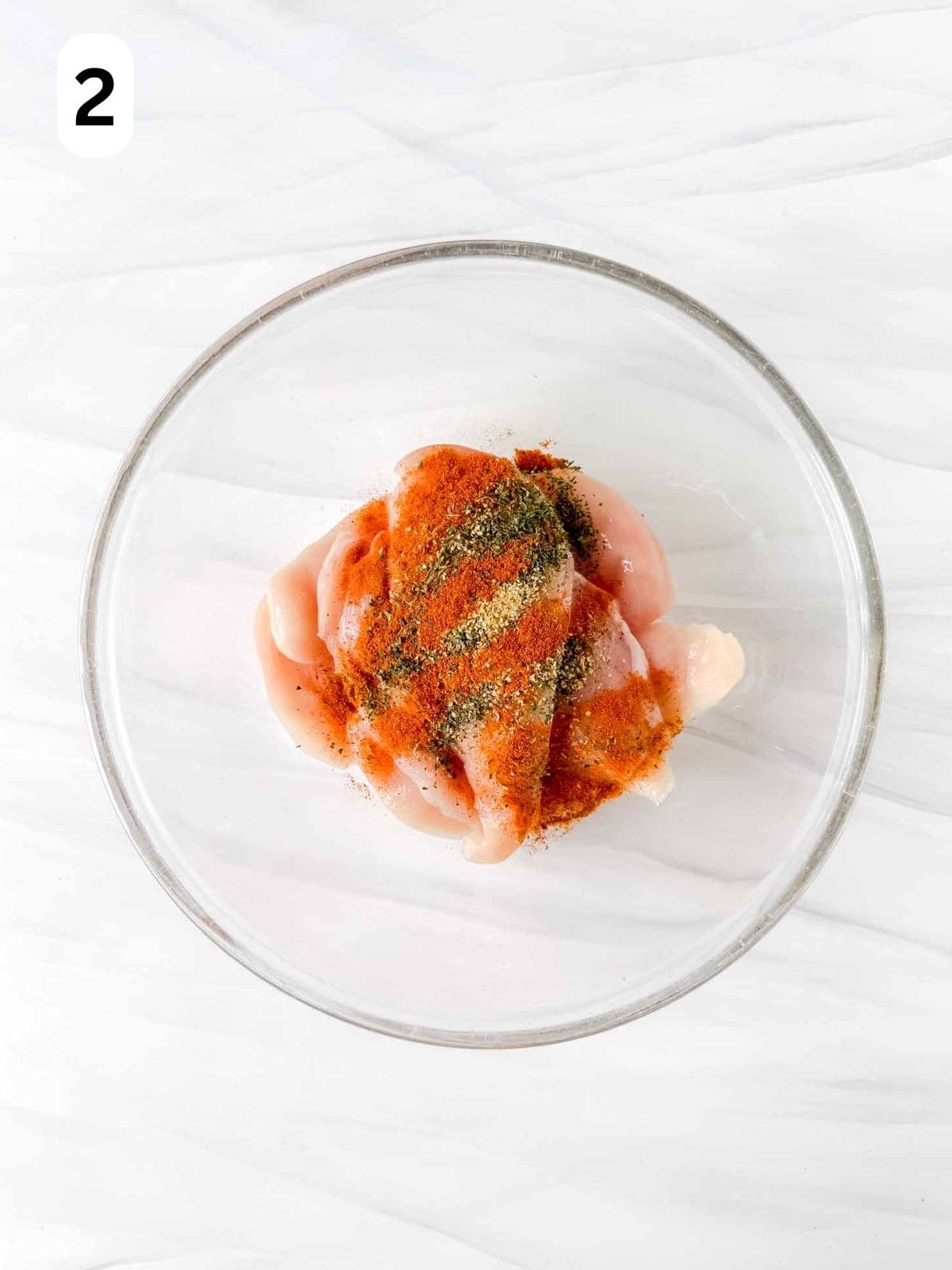 thin chicken breast pieces in a large glass bowl with paprika and herbs labelled number two.