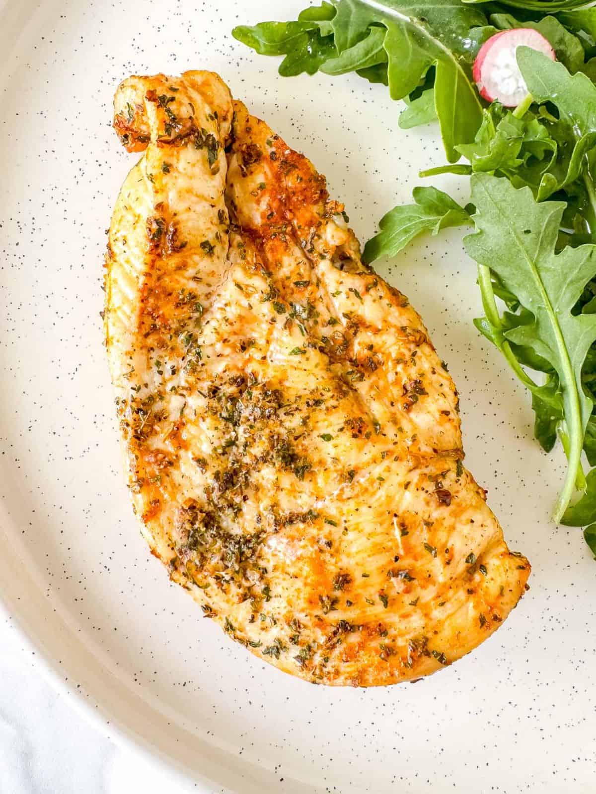 air fryer thinly sliced chicken breast on a plate with arugula salad.