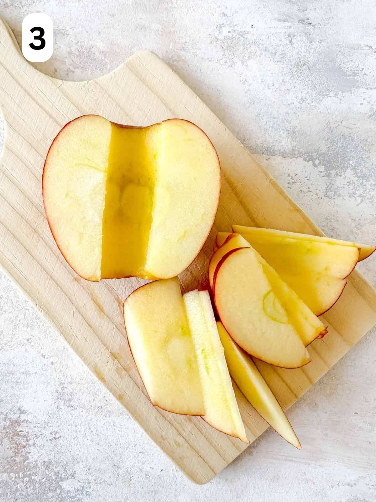 sliced apple on a wooden board labelled number three.