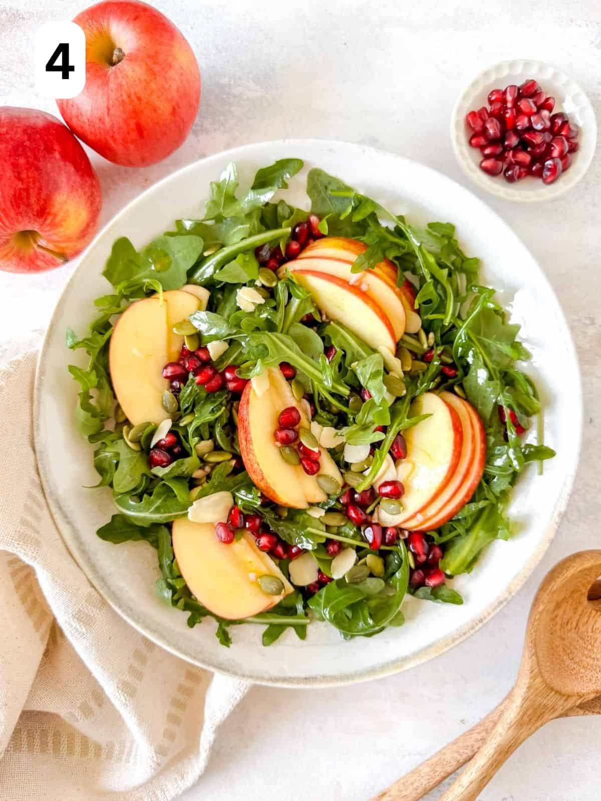 apple and pomegranate salad in a white bowl next to red apples labelled number four.