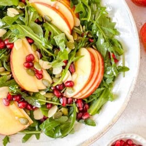 apple and pomegranate salad in a white bowl next to red apples.