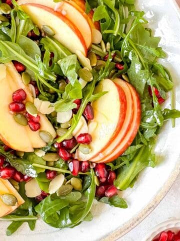 apple and pomegranate salad in a white bowl next to red apples.