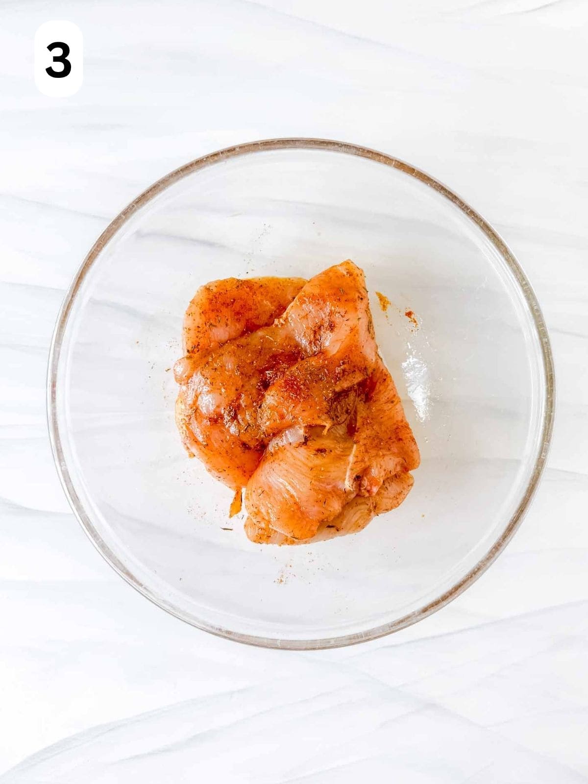 thin sliced chicken breasts coated in oil, herbs and spice in a glass bowl labelled number three.