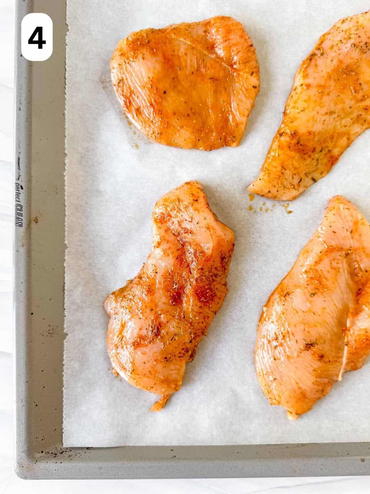 four pieces of thin sliced chicken breast on a lined baking sheet labelled number four.