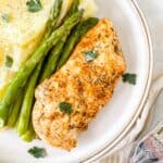 oven baked thin sliced chicken breast on a plate with asparagus and mashed potato garnished with fresh parsley.