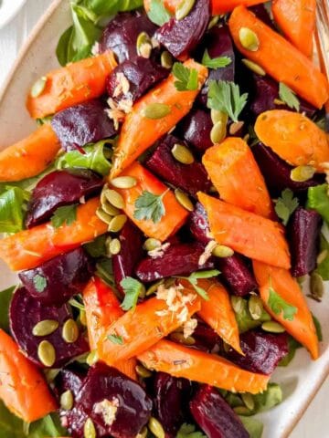 beet and carrot salad on a white plate garnished with fresh herbs and pumpkin seeds.