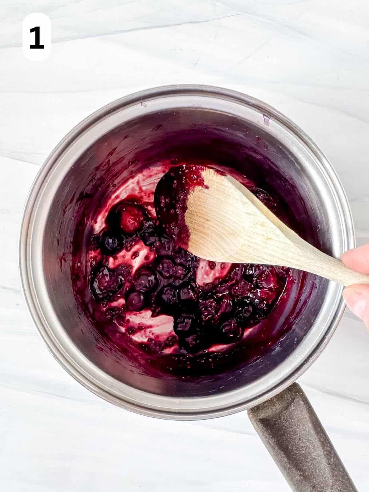 cooked blueberries in a pot being stirred with a wooden spoon labelled number one.