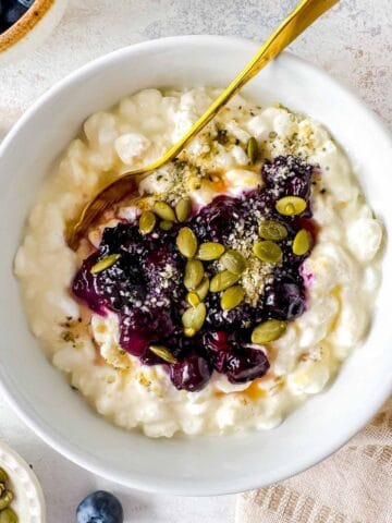 blueberry cottage bowl in a white bowl with a spoon topped with seeds.