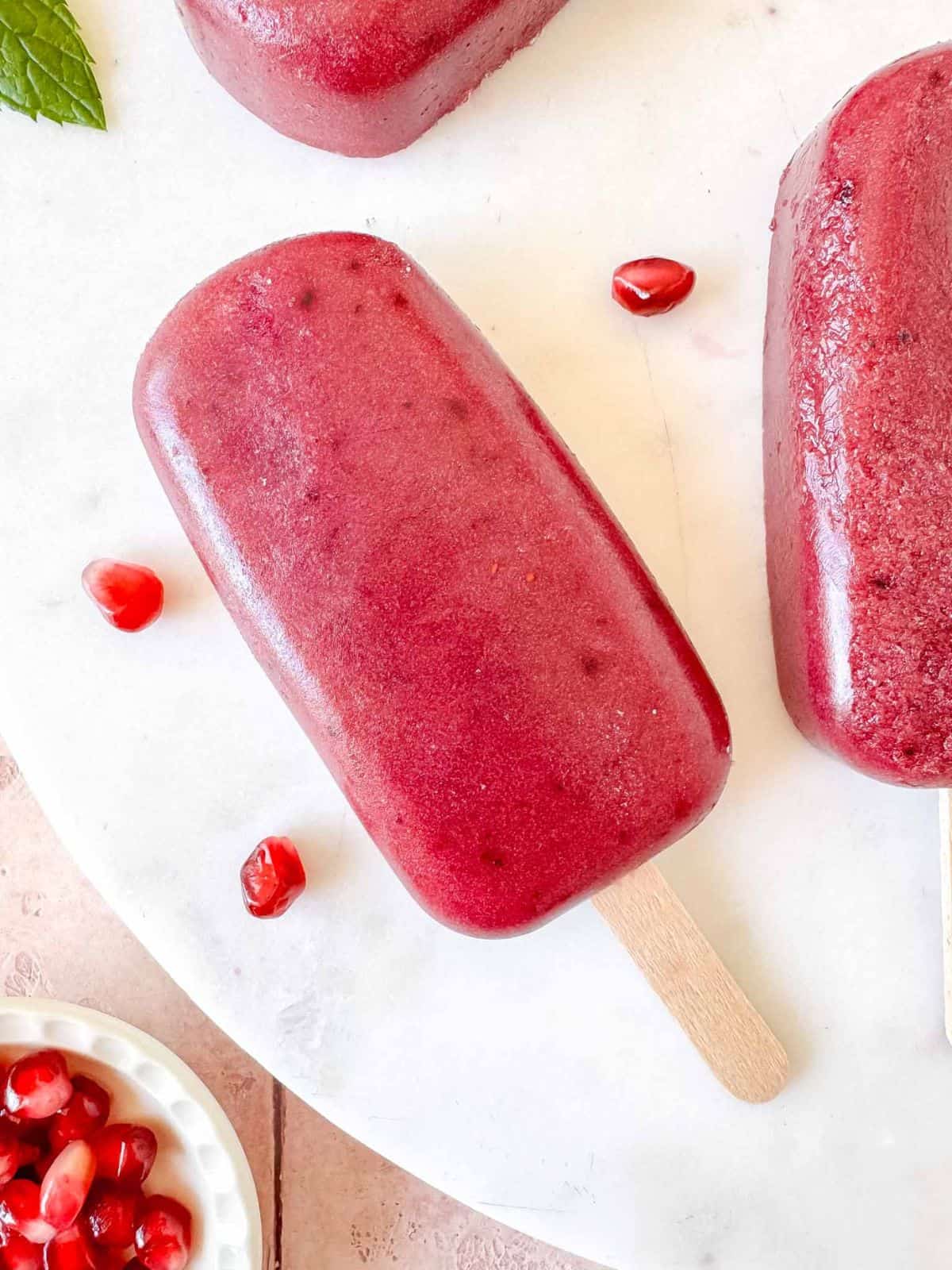 blueberry pomegranate popsicles on a white background next to fresh pomegranate seeds.