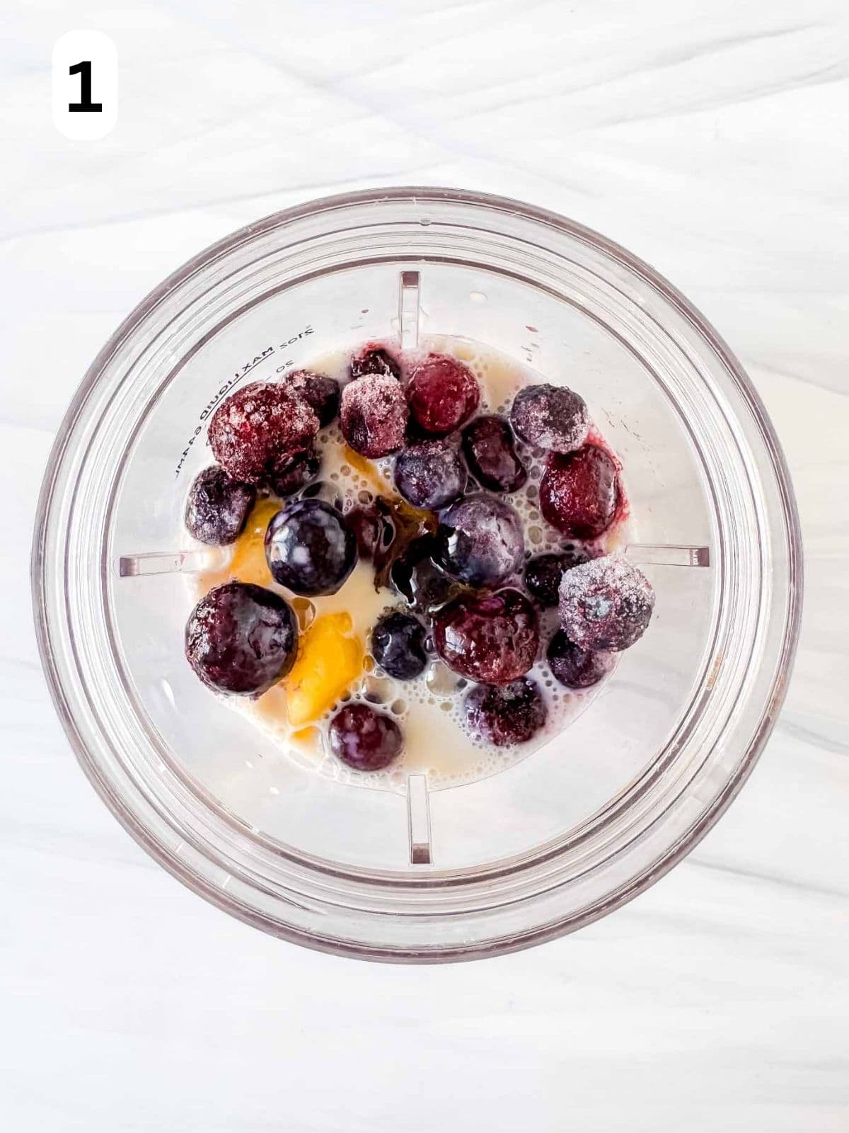 frozen fruits in a blender cup with plant milk and maple syrup labelled number one.