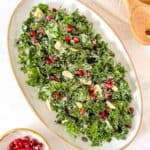 kale and pomegranate salad on a white plate next to a small bowl of pomegranate seeds.