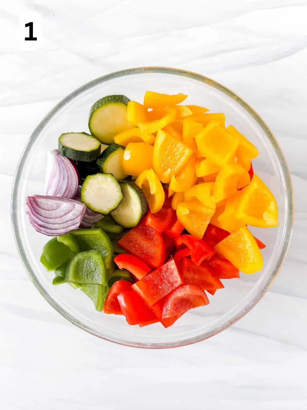 diced red, yellow and green bell peppers, zucchini and red onion in a glass bowl labelled number one.