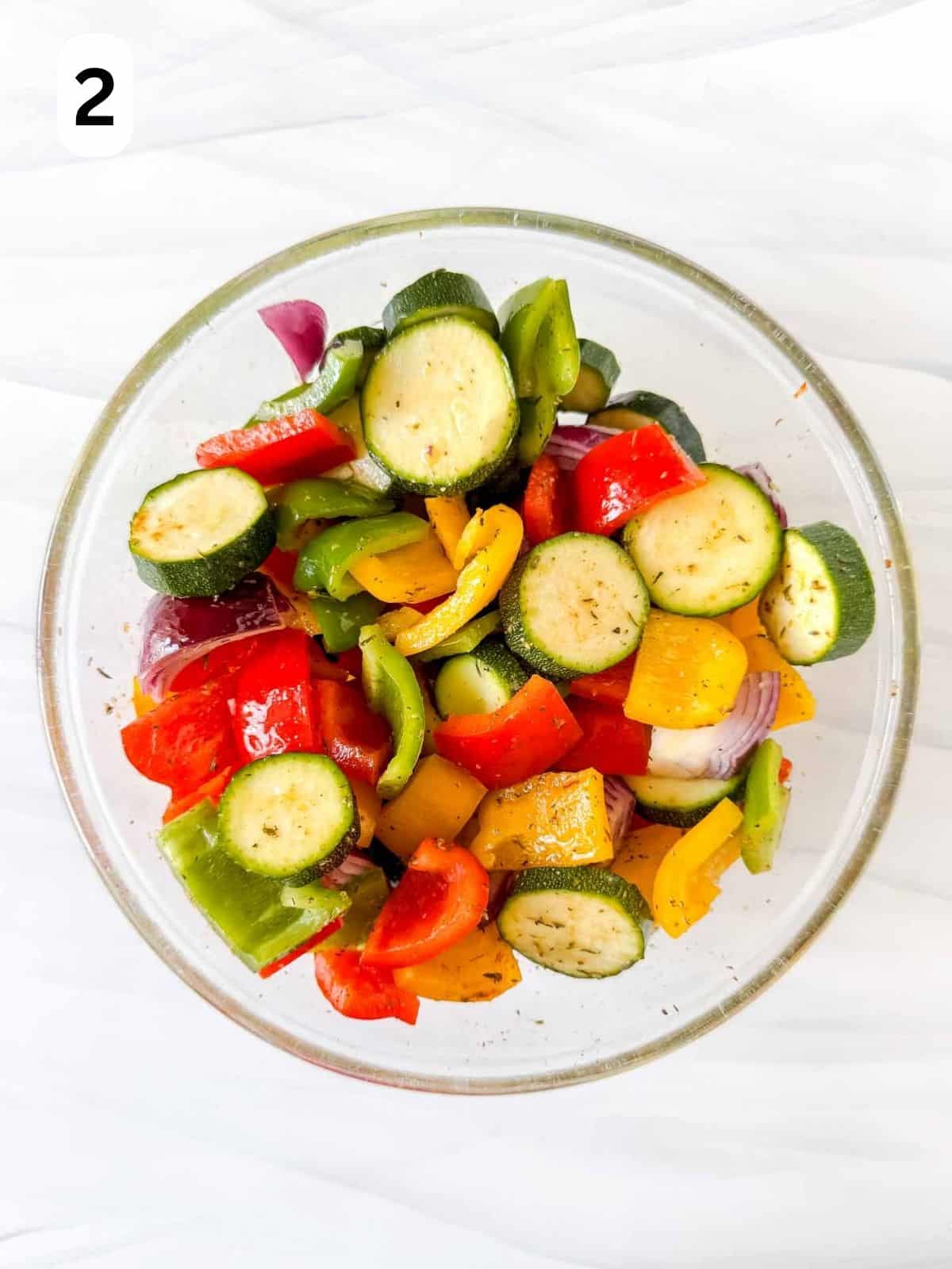 mixed vegetables coated in olive oil, herbs and spices in a glass bowl labelled number two.
