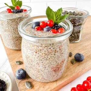 chia and flaxseed pudding in two glass jars topped with fruit and mint leaves.