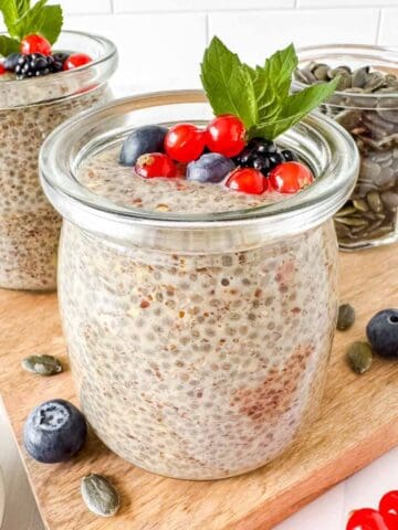 chia and flaxseed pudding in two glass jars topped with fruit and mint leaves.