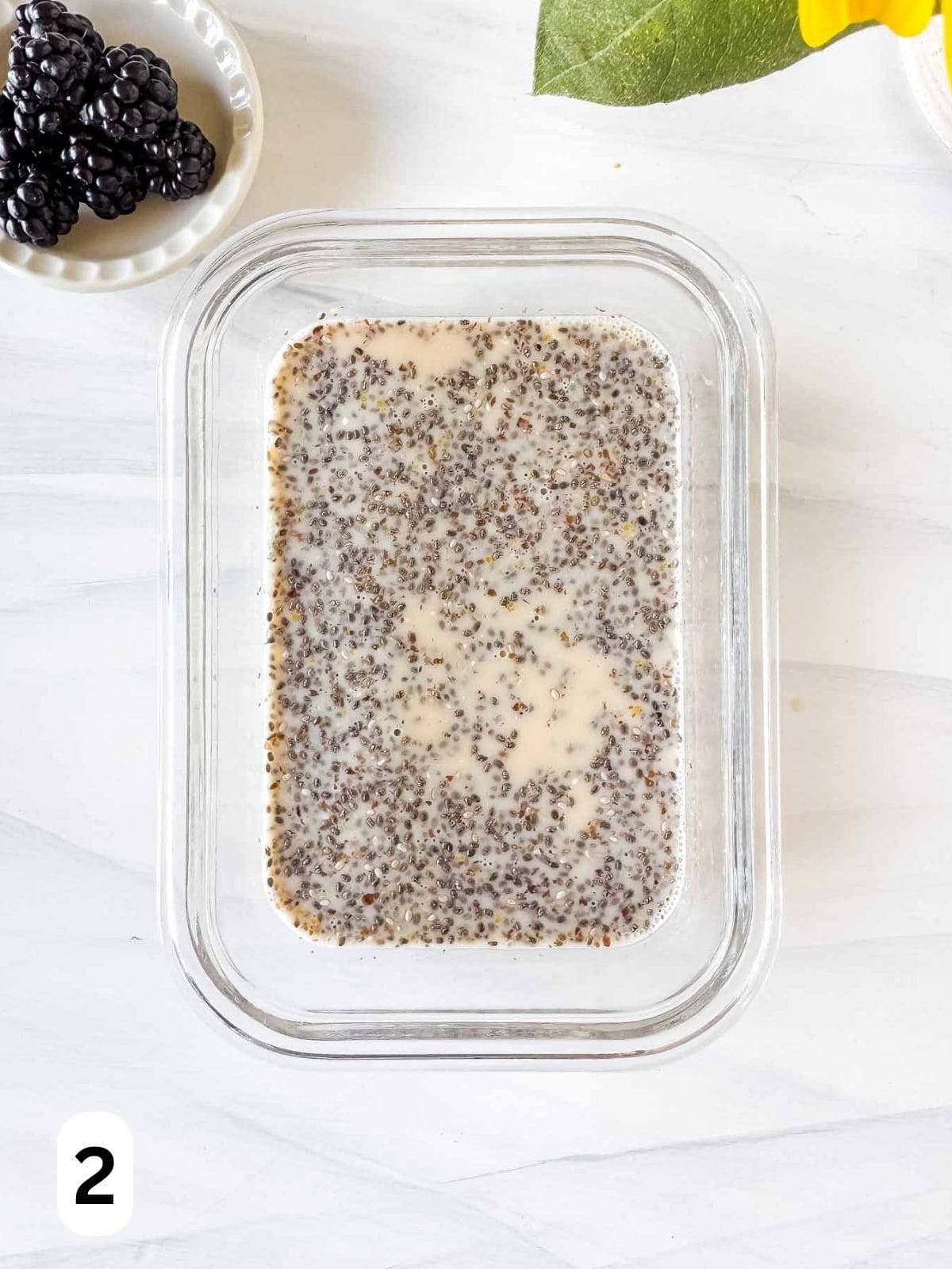 chia seeds, ground flaxseeds and maple syrup soaking in plant milk in a glass dish labelled number two.