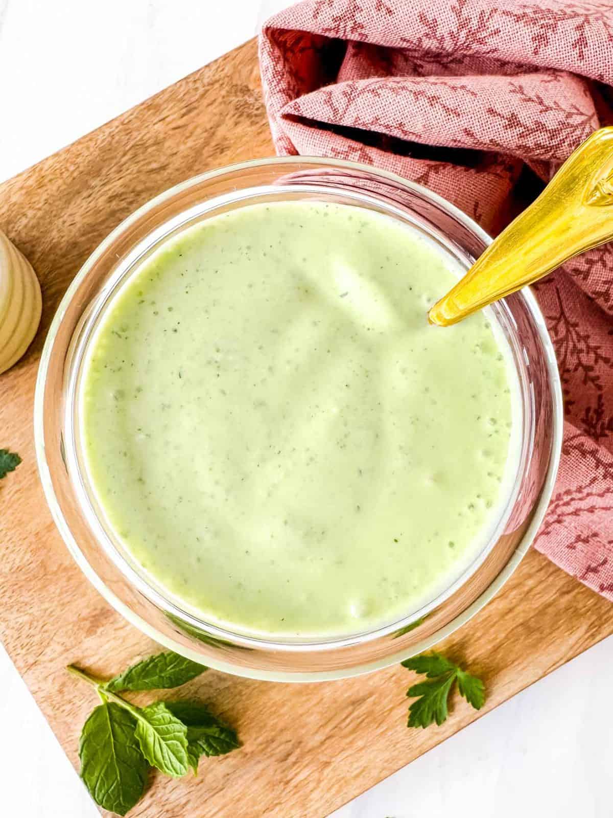 cottage cheese dressing in a glass jar with a spoon in it next to fresh herbs and a pink tea towel.