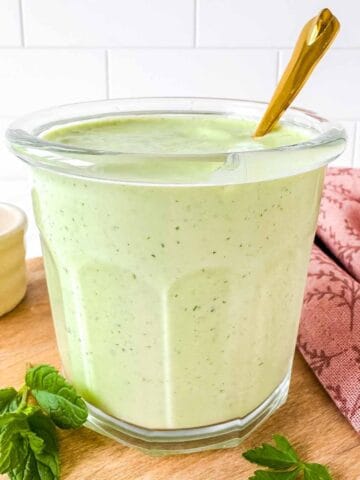 cottage cheese salad dressing in a glass jar with a spoon in it next to fresh herbs.