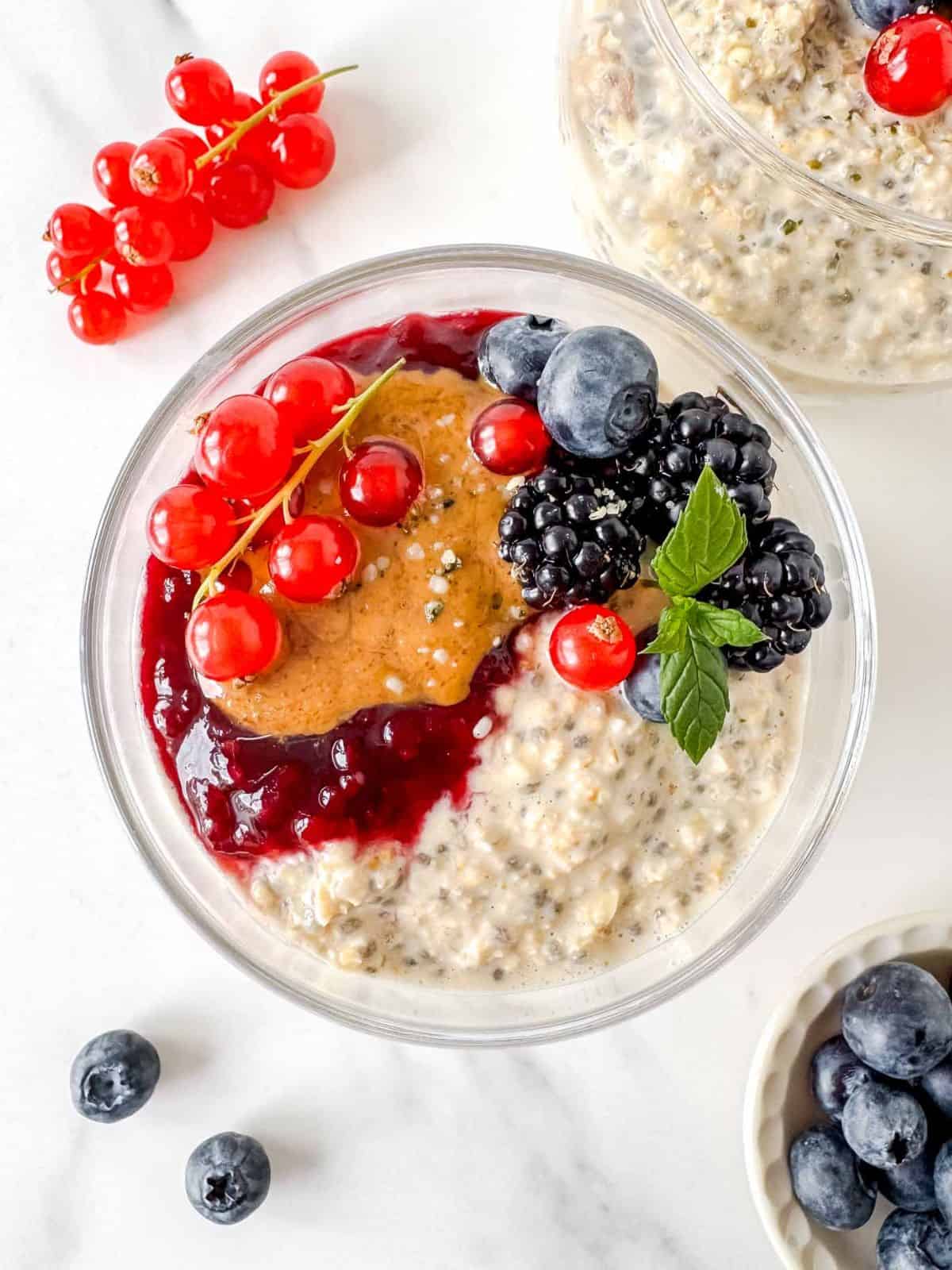 oatmeal chia pudding in two glasses topped with fruit, jam and nut butter.