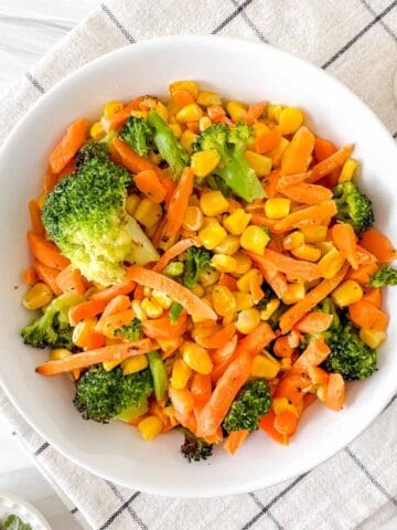 air fryer frozen vegetables in a white bowl on a checked cloth.