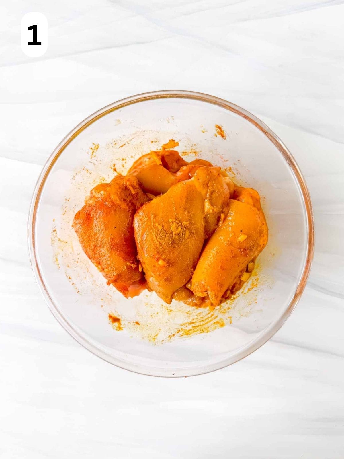 chicken thighs coated in turmeric and spice mix in a glass bowl labelled number one.