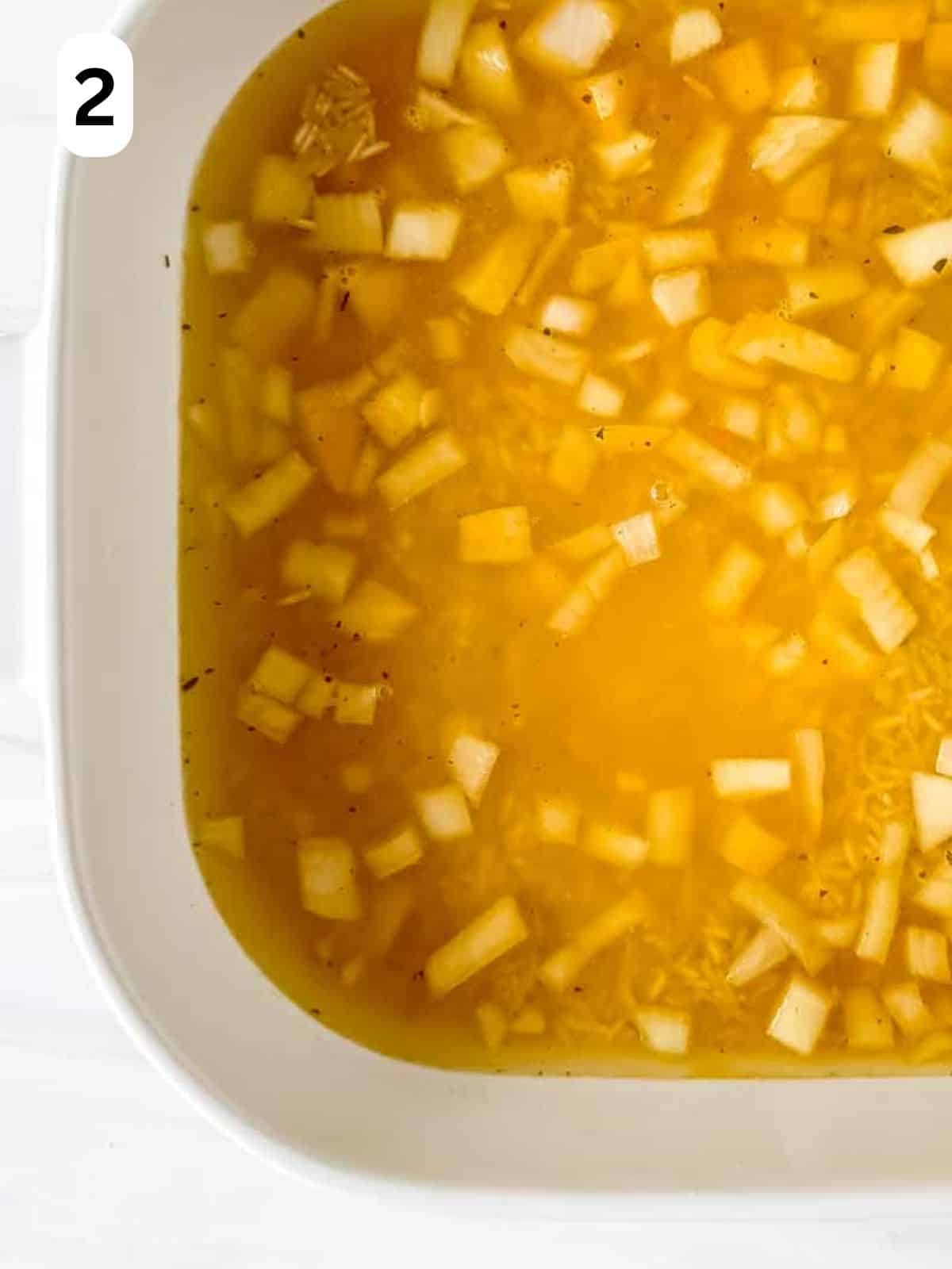 diced onion, rice, turmeric and stock in a white casserole dish labelled number two.