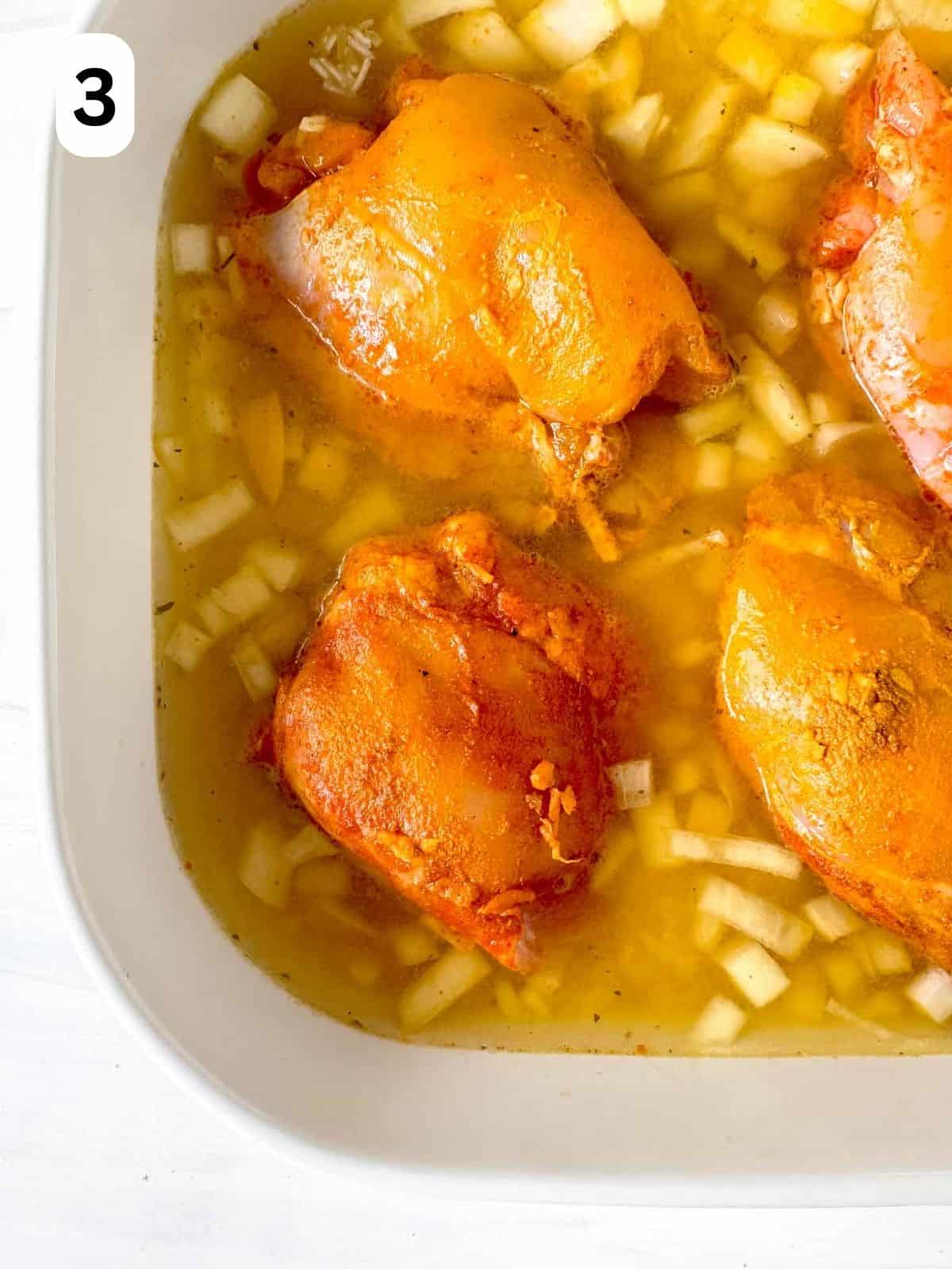 turmeric chicken thighs in onion, turmeric and stock in a white casserole dish labelled number three.