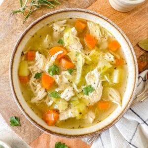 chicken soup without noodles in a light brown bowl next to fresh herbs.