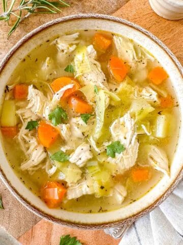 chicken soup without noodles in a light brown bowl next to fresh herbs.
