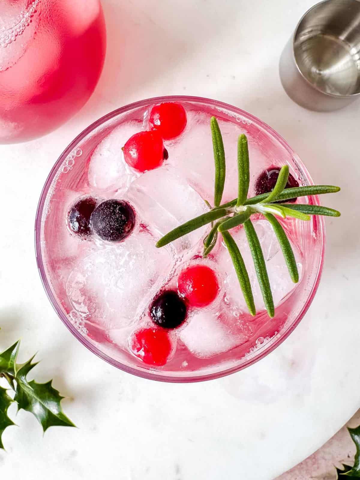 cranberry juice mocktail in a glass topped with ice and a rosemary sprig.