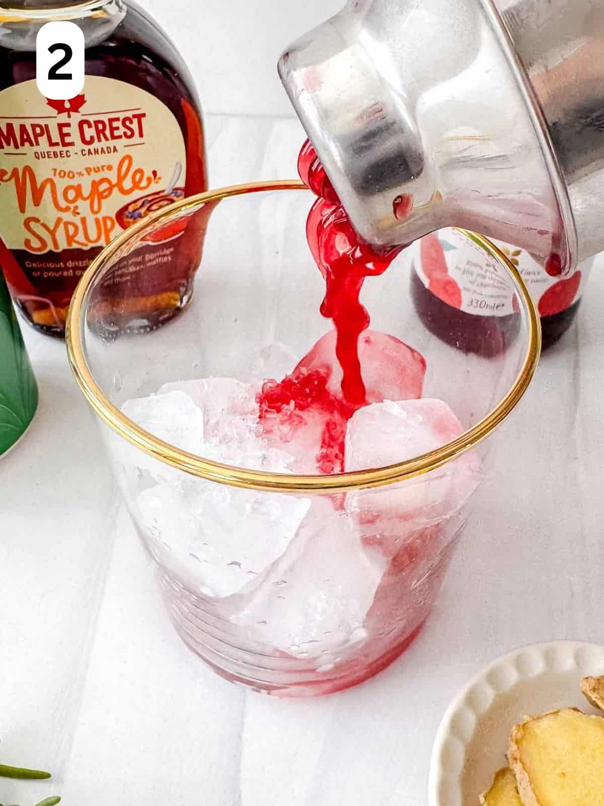 cranberry juice being poured into a glass filled with ice from a cocktail shaker labelled number two.
