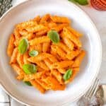 roasted red pepper pasta in a bowl garnished with fresh basil leaves.