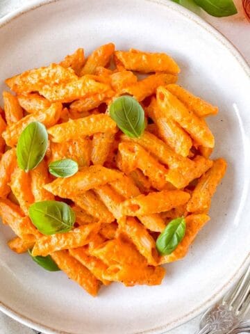 roasted red pepper pasta in a bowl garnished with fresh basil leaves.