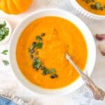 roasted butternut squash and carrot soup in a white bowl garnished with parsley and pumpkin seeds.