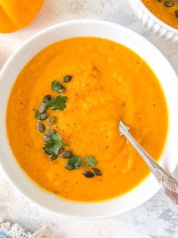 roasted butternut squash and carrot soup in a white bowl garnished with parsley and pumpkin seeds.