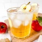 apple juice mocktail in a glass next to red apples.