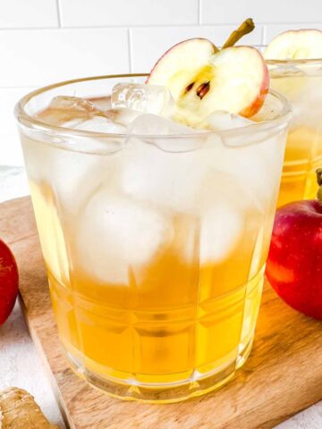 apple juice mocktail in a glass next to red apples.