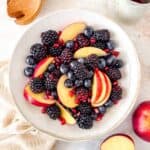 fall fruit salad of red apple slices, blackberries, blueberries and pomegranate seeds in a bowl.