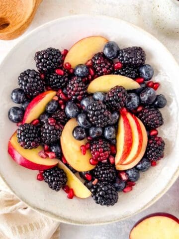 fall fruit salad of red apple slices, blackberries, blueberries and pomegranate seeds in a bowl.