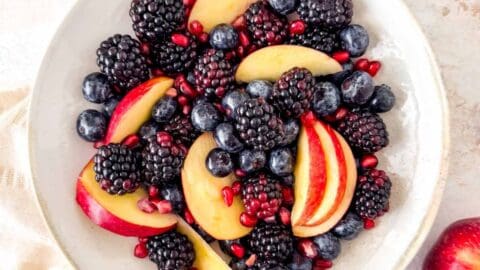 fall fruit salad of red apple slices, blackberries, blueberries and pomegranate seeds in a bowl.